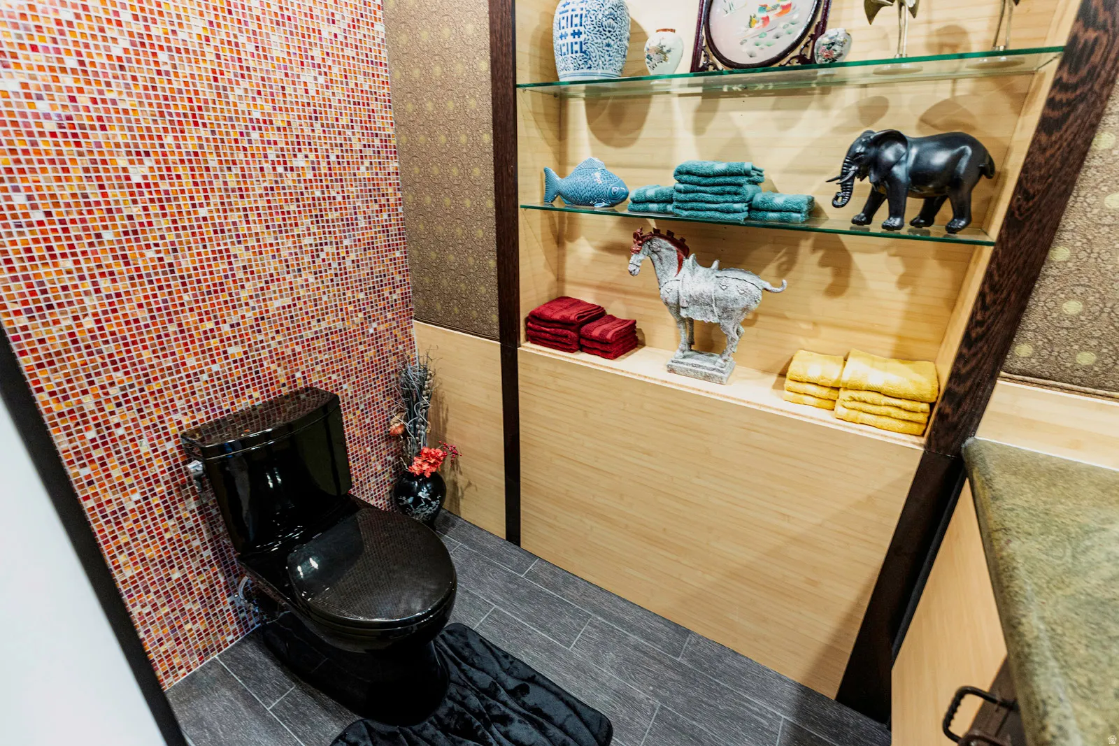 Powder room featuring a black toilet, mosaic tile accent wall, wood-finish flooring, and built-in shelving with glass shelves