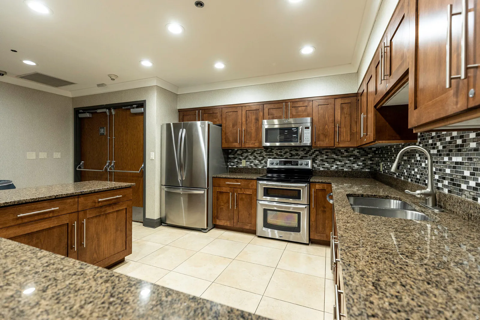 Well-appointed kitchen featuring granite countertops, a mosaic tile backsplash, stainless steel appliances, and extensive wood cabinetry