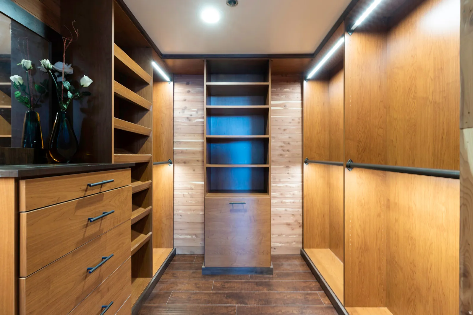 Custom walk-in closet featuring wood-finish cabinetry, built-in shelving, integrated lighting, dark wood-finish flooring, and a stone-look countertop