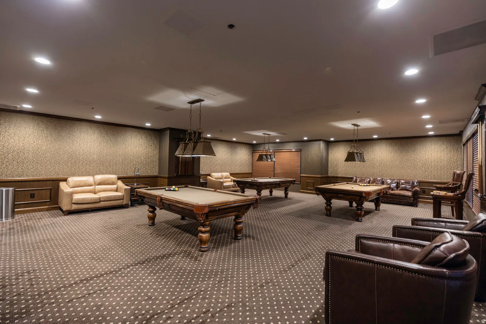 Spacious recreation area featuring patterned carpet flooring, recessed lighting, wall sconces, and crown molding