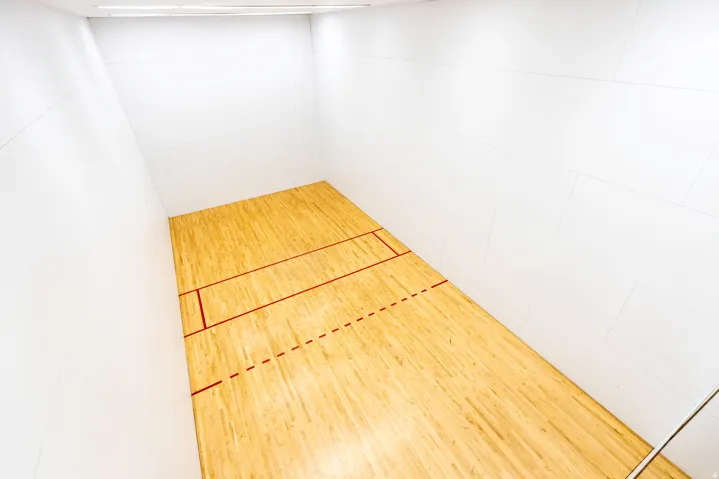 Indoor racquetball court with light wood-finish flooring and marked red lines