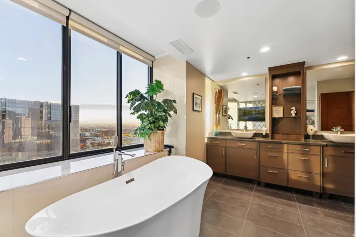 Contemporary bathroom featuring a freestanding soaking tub, expansive window, dual vanity with vessel sinks, built-in shelving, and tile flooring