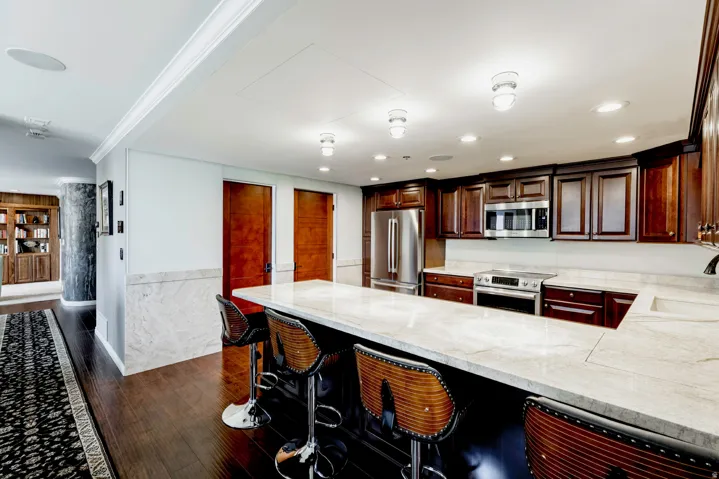 Gourmet kitchen featuring rich wood cabinetry, stainless steel appliances, a spacious central island with an integrated sink, and recessed lighting