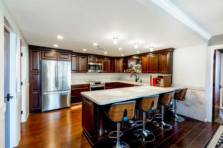 Spacious kitchen featuring rich wood cabinetry, stainless steel appliances, light-toned countertops, a multi-person island, and dark wood-finish flooring