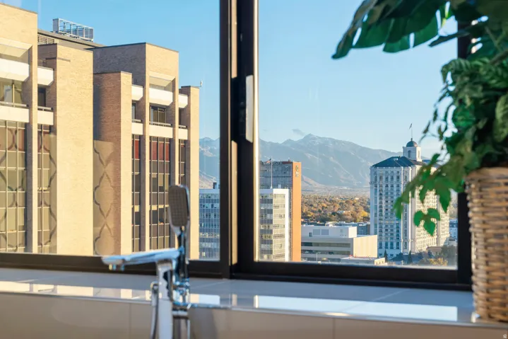 Soaking tub with floor-mounted chrome faucet, set against a expansive window offering cityscape and mountain scenery