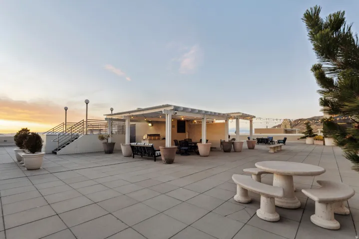 Expansive rooftop patio featuring a built-in outdoor kitchen, multiple covered pergola areas, and concrete paver flooring