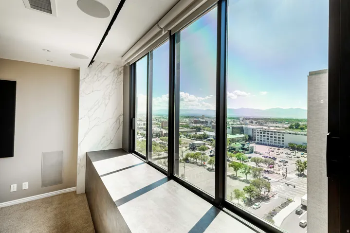 Floor-to-ceiling windows with roller shades offer expansive city and mountain scenery