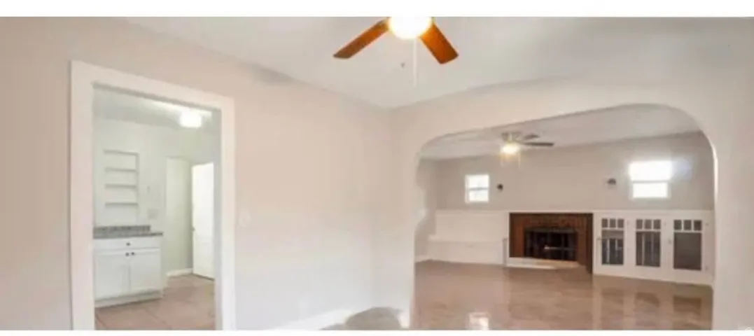 Living area with an arched doorway, wood-finish flooring, ceiling fan, and a fireplace with a brick surround