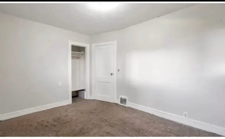 Neutral-toned room featuring light gray walls, brown carpet, white trim, and a built-in closet with shelving and hanging rods