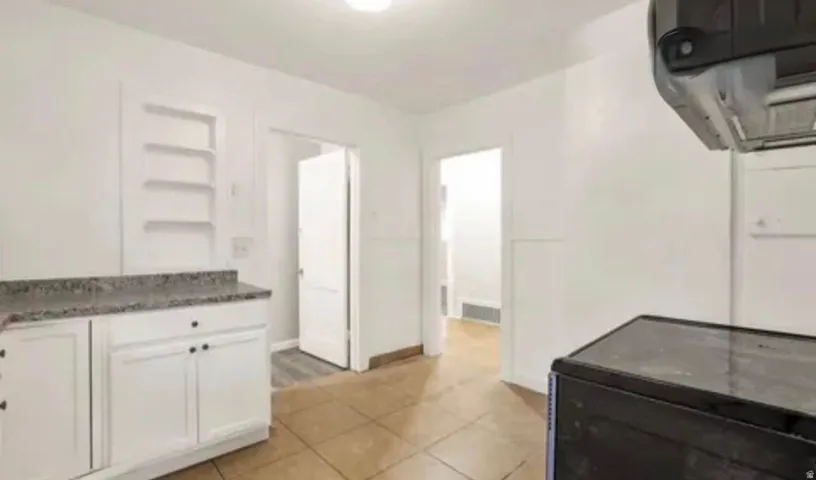 Kitchen featuring white cabinetry with dark hardware, a speckled countertop, and built-in shelving