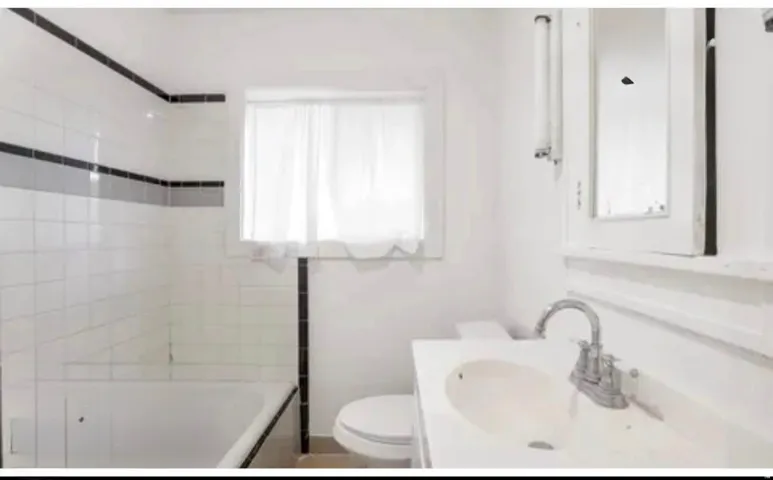 Bathroom featuring a white tile surround bathtub, a single window, and a vanity with an integrated sink and chrome faucet
