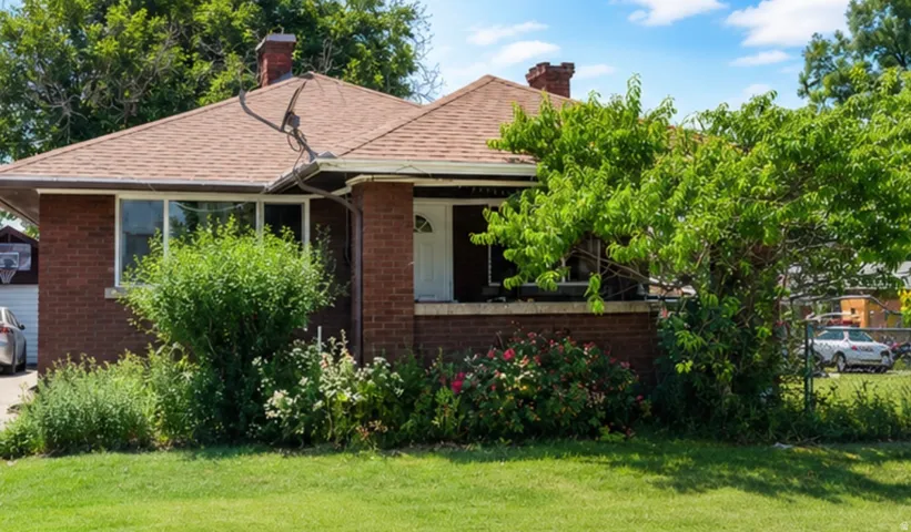 Brick exterior with a peaked shingle roof, featuring mature front landscaping and a covered entry