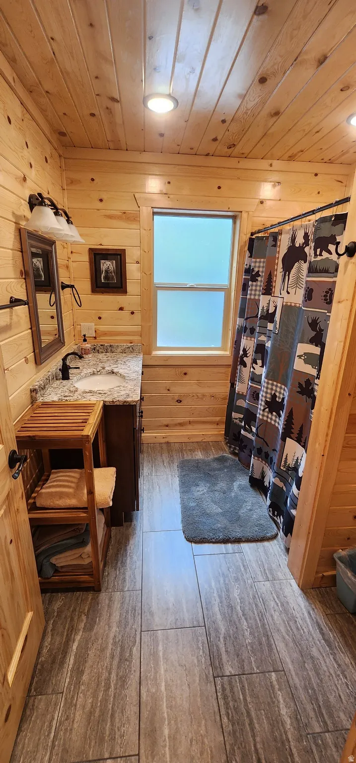 Bathroom with plank wood walls and ceiling, a single vanity with a granite countertop, and a shower area