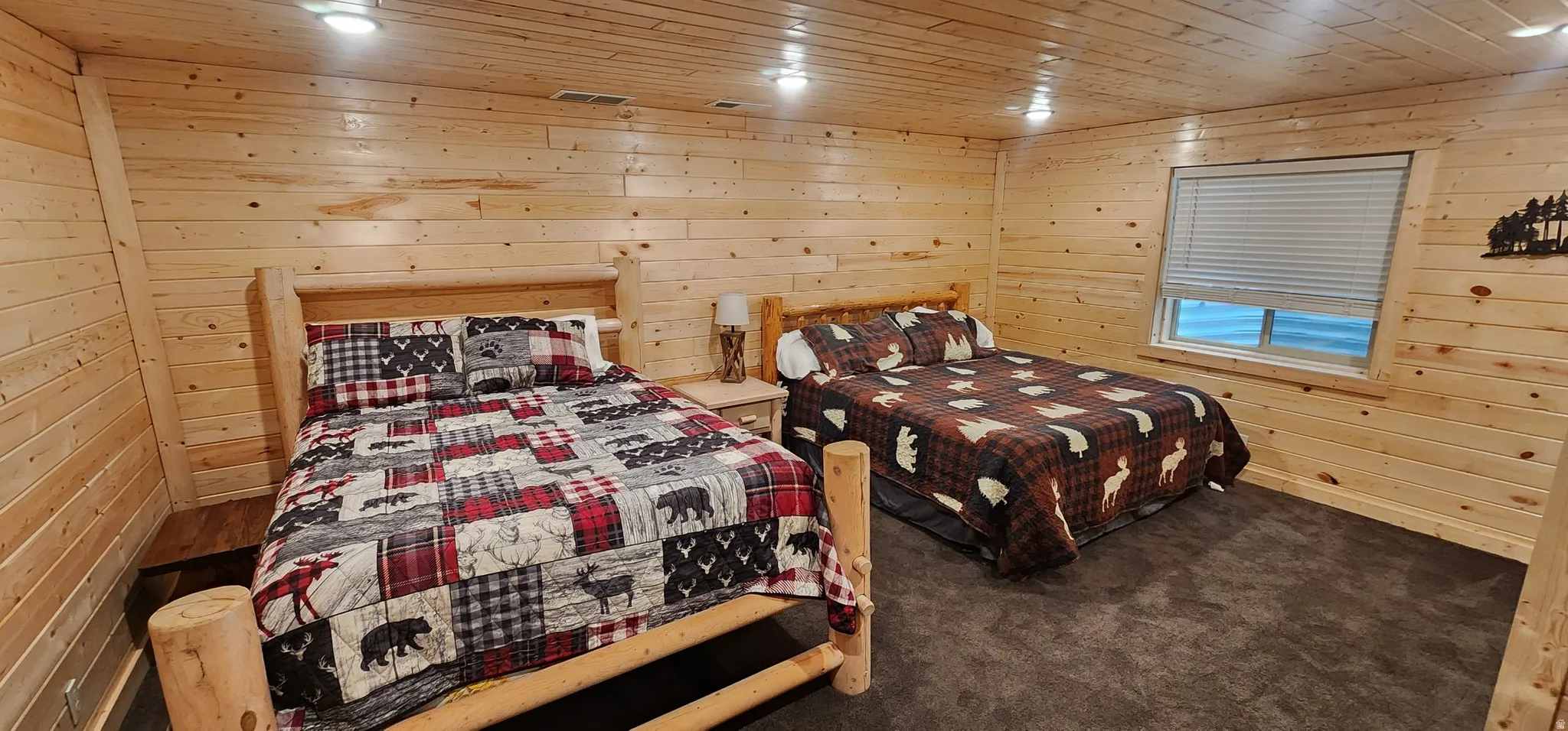 Spacious interior featuring full wood-panel walls and ceilings, two wood-frame beds, dark carpeting, and a window with horizontal blinds