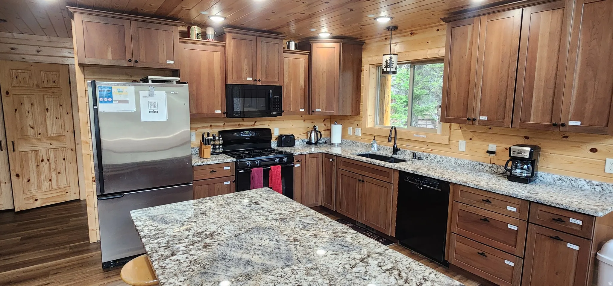 Kitchen featuring wood-finish cabinetry, granite countertops, stainless steel refrigerator, black range, and black dishwasher