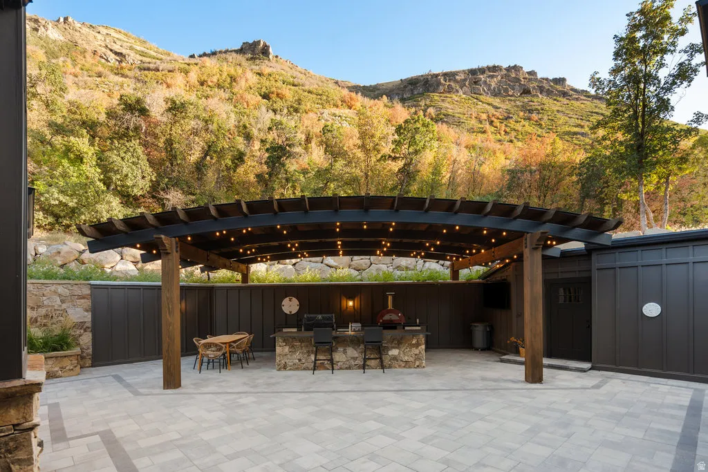 Spacious patio area with paver flooring and a curved pergola featuring string lighting