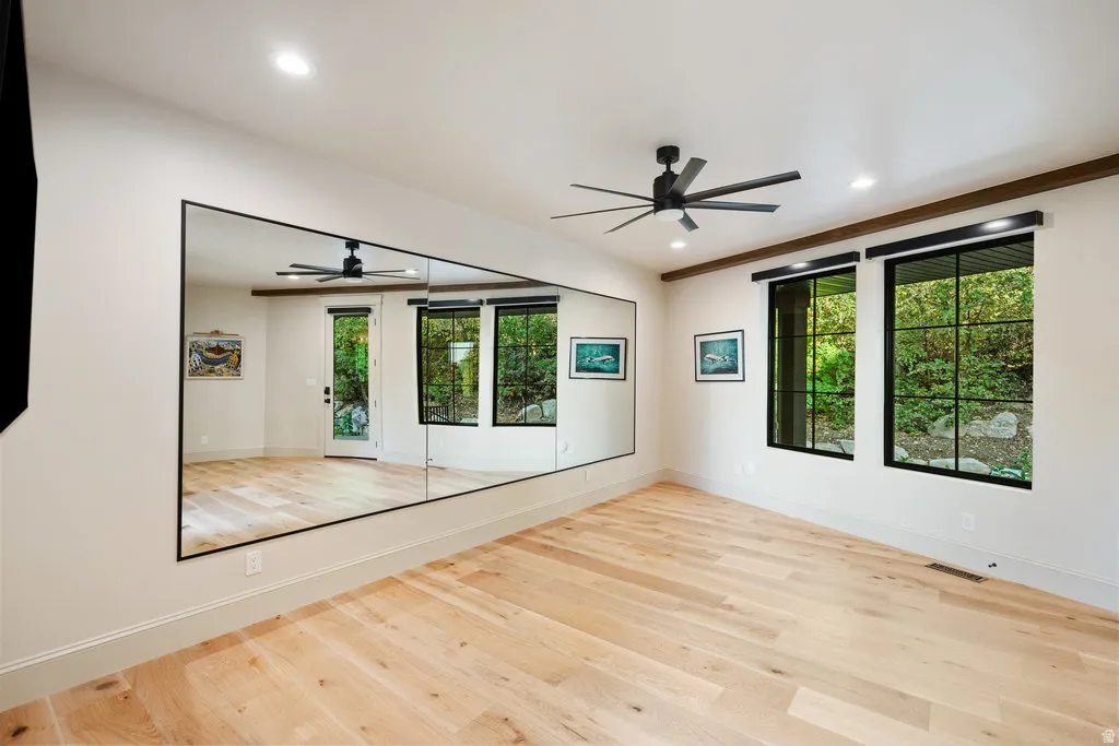 Spacious room featuring light wood-finish flooring, a wall-mounted mirror, and black-framed windows