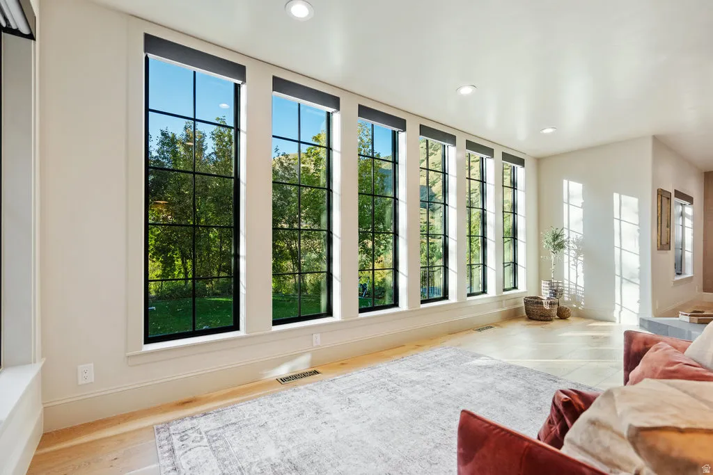 Interior space featuring a bank of tall, grid-patterned windows with dark frames, light-colored walls, recessed lighting, light wood-finish flooring, and white baseboards
