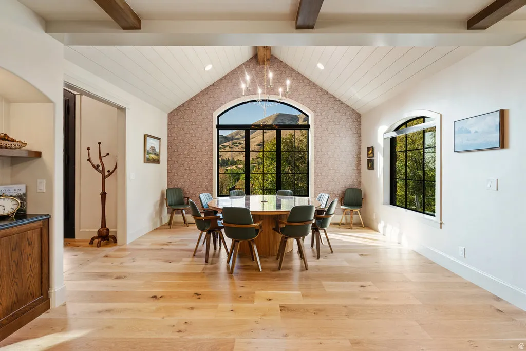 Spacious dining room featuring vaulted ceilings with exposed wood beams, light wood-finish flooring, and a large arched window with black framing