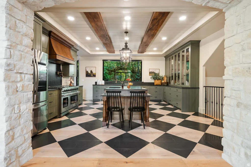 Gourmet kitchen featuring a large central island, professional-grade range with a custom wood hood, built-in refrigerator, checkerboard flooring, and exposed ceiling beams
