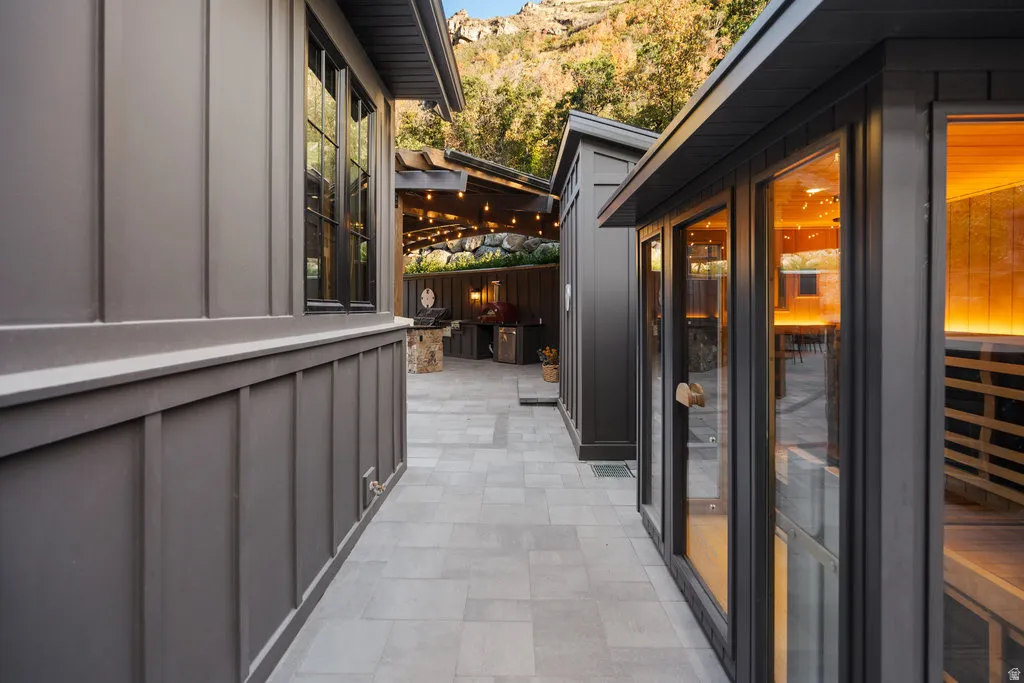 Exterior courtyard featuring paver flooring, modern board and batten siding, multiple buildings with dark-framed windows, and an outdoor kitchen area with string lighting
