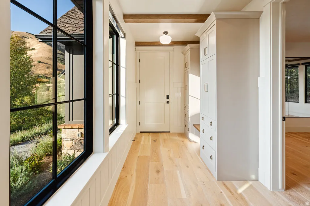 Entryway featuring multiple floor-to-ceiling windows with black frames, wood-finish flooring, two built-in storage units with cabinet and drawer space, an overhead light fixture, and exposed wood beams