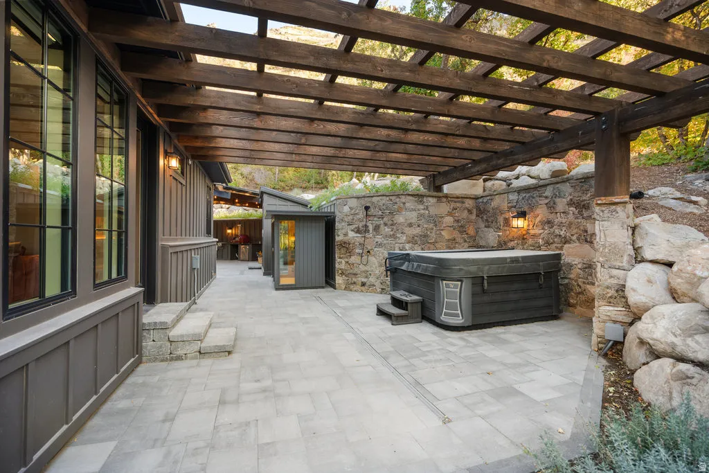 Expansive stone paver patio featuring a wooden pergola overhead and a built-in hot tub