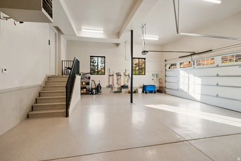 Spacious garage with light-colored epoxy flooring, two overhead garage doors with frosted window panels, and interior stairs featuring a black metal railing