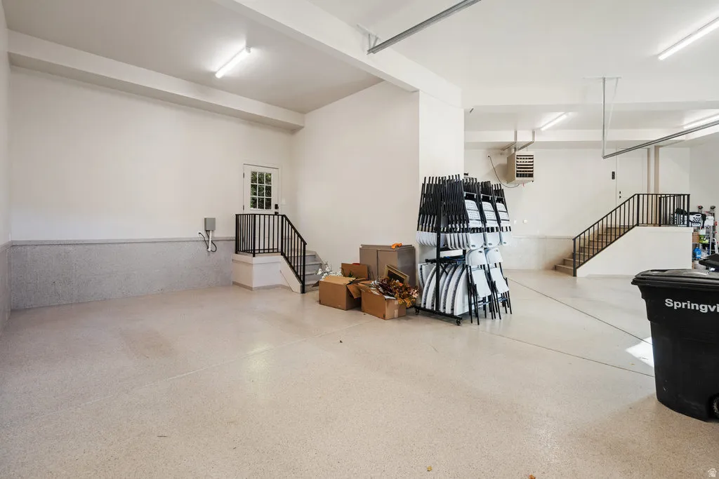 Spacious garage with an epoxy-finished floor, fluorescent lighting, and two distinct staircases with black metal railings