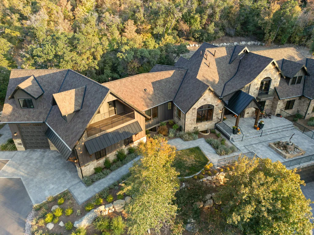 Expansive property featuring varied rooflines, stone and wood-look siding, multiple balconies, a large paver patio, and a built-in fire pit area