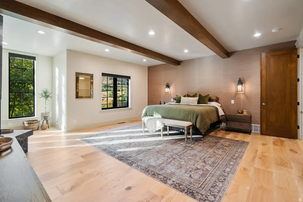 Spacious Primary bedroom featuring exposed wood beams, light wood-finish flooring, a textured accent wall, and recessed lighting