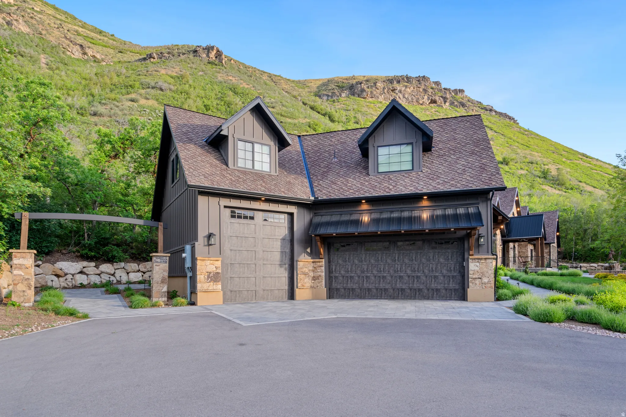 Exterior featuring board and batten siding, multiple garage doors, stone accents, and dormer windows