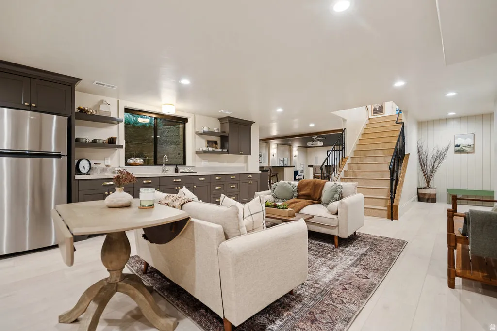 Open-concept living area featuring a full kitchen with stainless steel appliances, recessed lighting, wood-finish flooring, and a hardwood staircase with wrought iron balusters