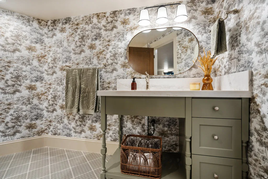 Vanity with an oval mirror, three-light fixture, and patterned wallpaper