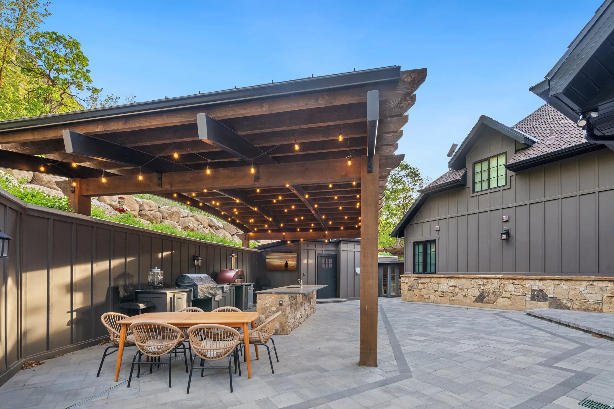 Expansive stone paver patio featuring a wooden pergola with string lighting