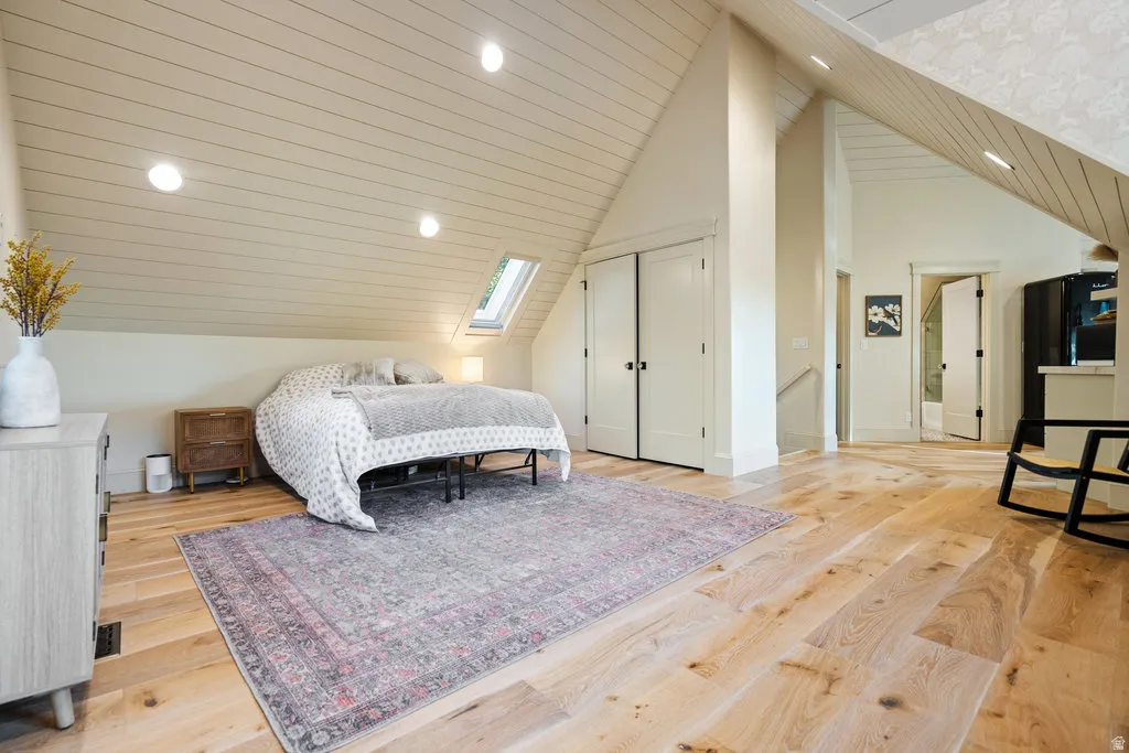 Spacious room featuring vaulted ceilings with wood-finish paneling, light wood-finish flooring, recessed lighting, double-door closet, and a skylight