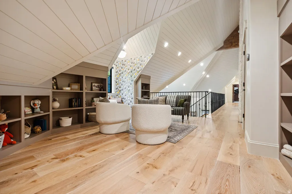 Spacious loft area featuring light wood-finish flooring, built-in shelving, vaulted shiplap ceilings with recessed lighting, and a black metal railing