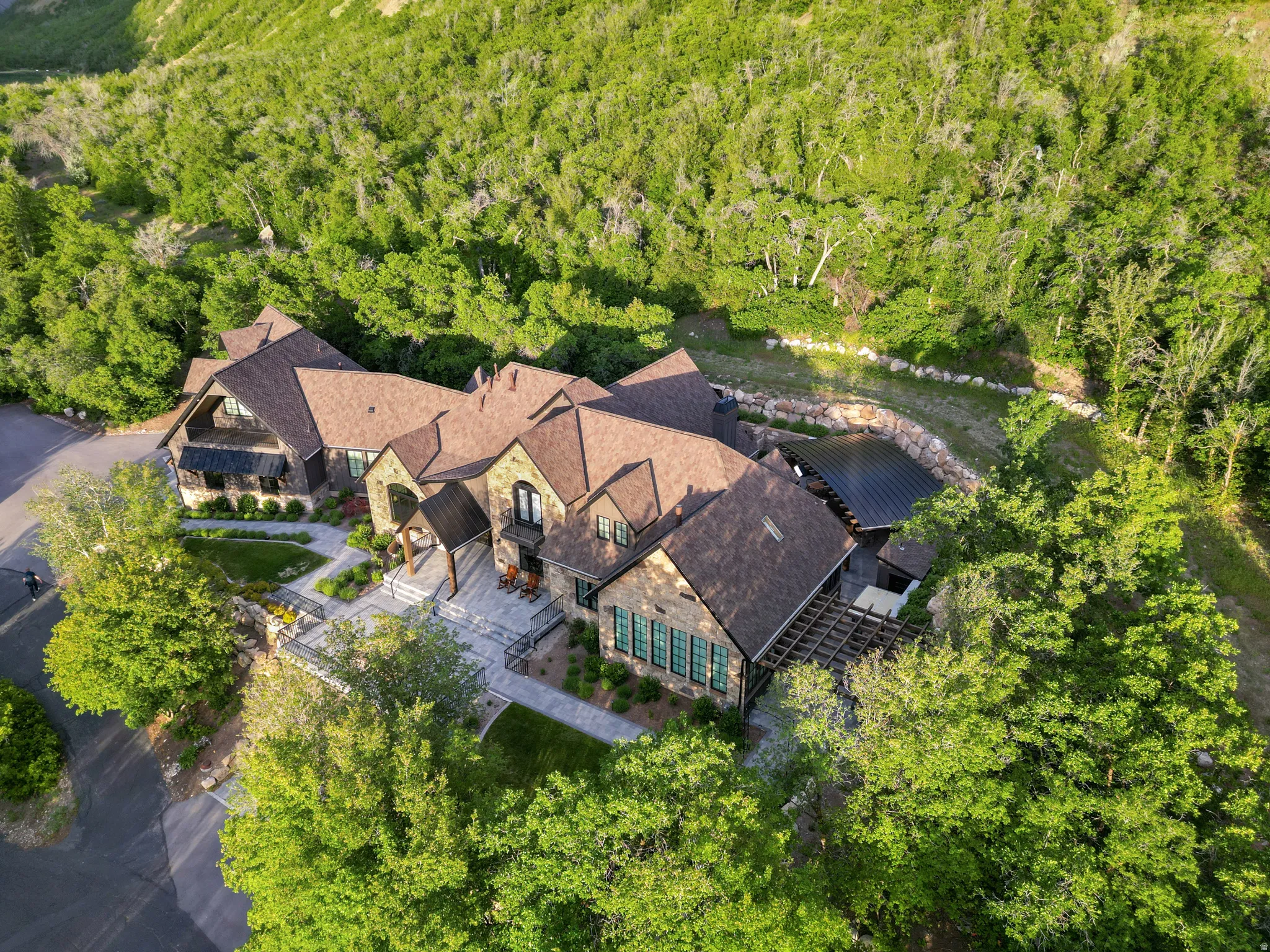Expansive multi-level stone residence featuring multiple gabled rooflines, dark-framed windows, and an integrated pergola