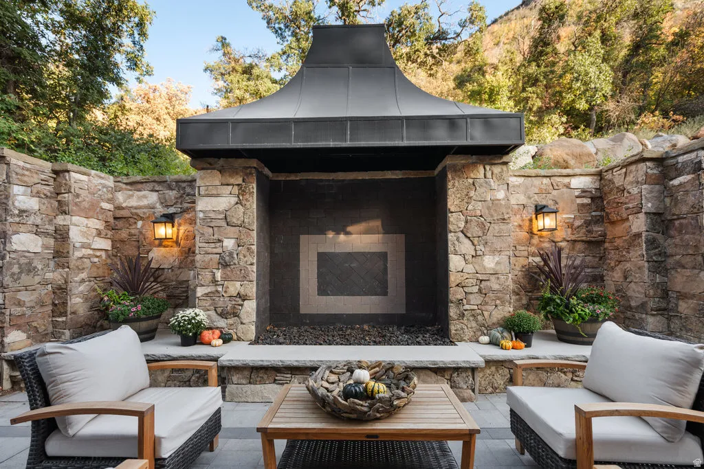 Outdoor stone fireplace with a fluted metal hood, flanked by stone walls and integrated lighting fixtures