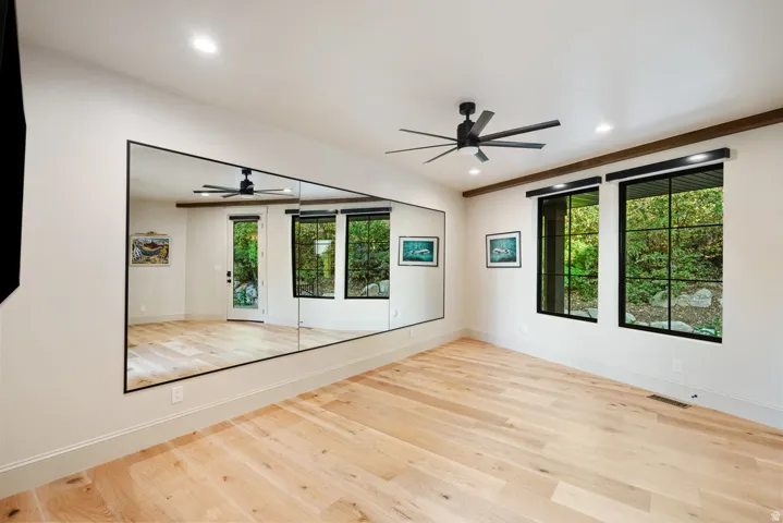 Spacious room featuring light wood-finish flooring, a wall-mounted mirror, and black-framed windows