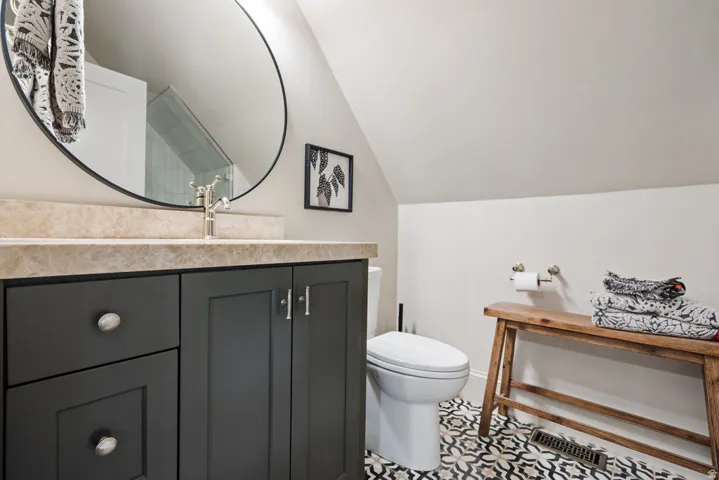 ADU Bathroom featuring a dark gray vanity with a light-colored countertop, an oval mirror, and patterned floor tiling