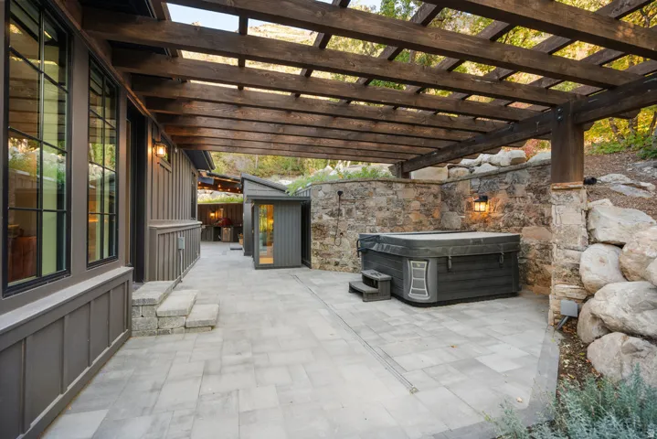Expansive stone paver patio featuring a wooden pergola overhead and a built-in hot tub
