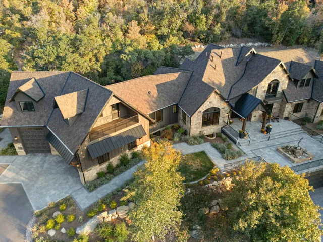 Expansive property featuring varied rooflines, stone and wood-look siding, multiple balconies, a large paver patio, and a built-in fire pit area
