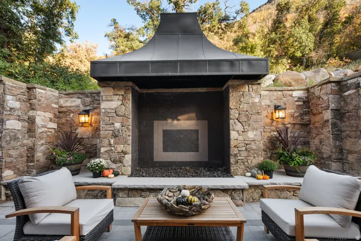 Outdoor stone fireplace with a fluted metal hood, flanked by stone walls and integrated lighting fixtures