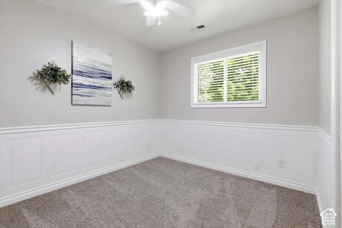 Spacious room featuring panel wainscoting, light grey wall paint, and plush carpet flooring