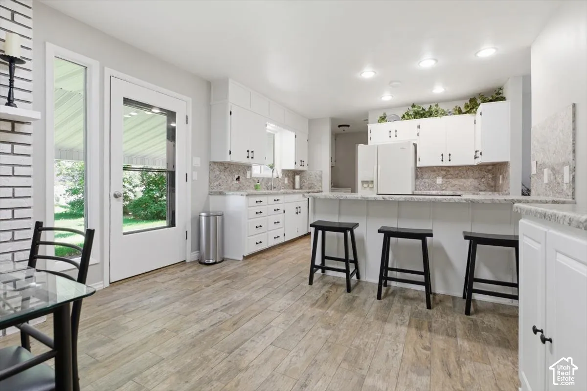 Kitchen featuring wood-finish flooring, white cabinetry, integrated refrigerator, and a breakfast bar with stone-finish countertops