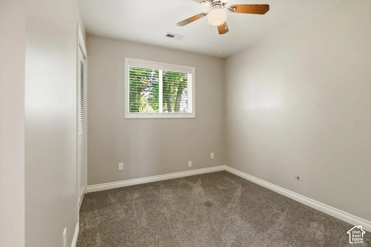 Carpeted room with a window featuring white horizontal blinds, a ceiling fan with integrated lighting, and neutral wall paint