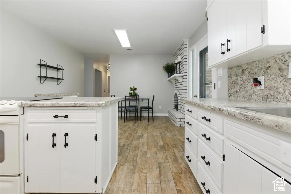 Kitchen area featuring white cabinetry with black hardware, stone-look countertops, and a coordinating backsplash