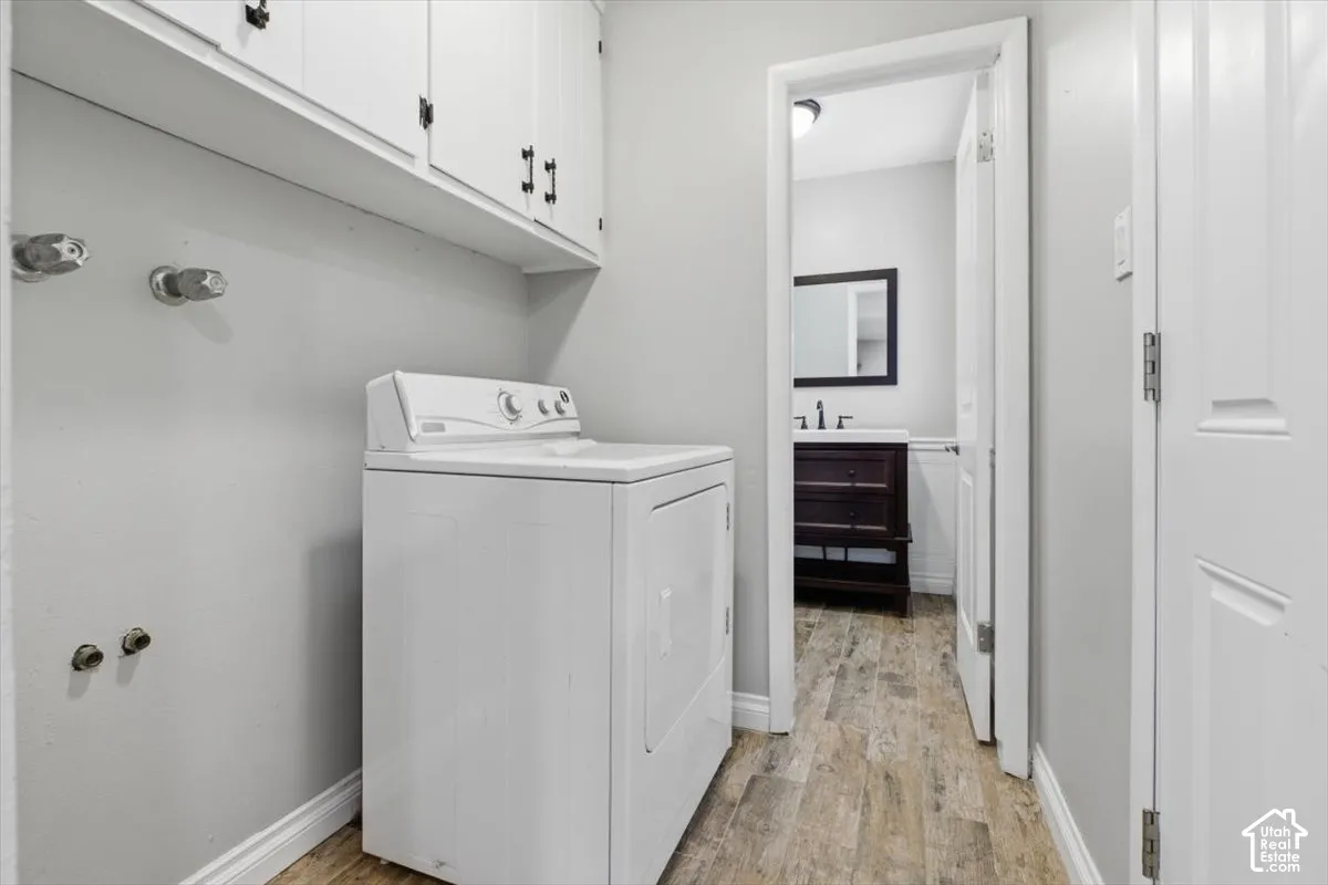 Laundry area featuring built-in white cabinetry, light gray walls, and wood-finish flooring