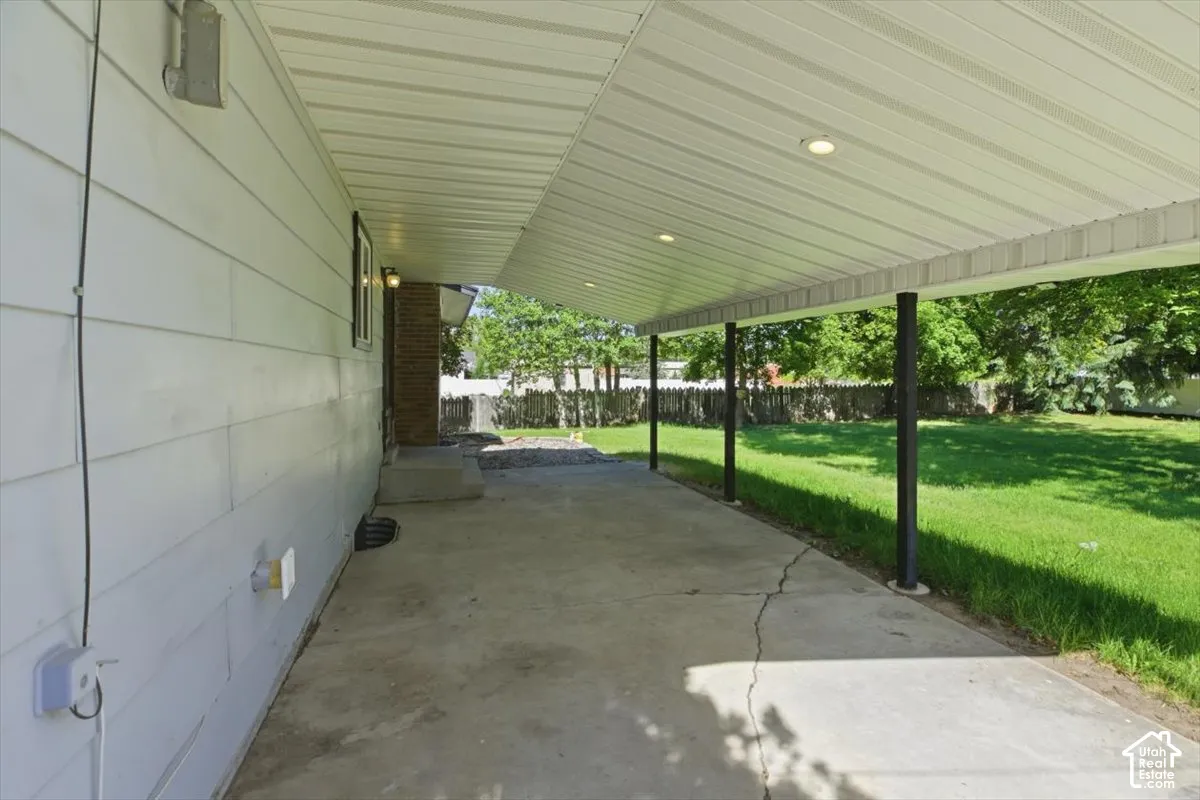 Covered concrete patio extending along the home's siding, featuring recessed lighting and support columns